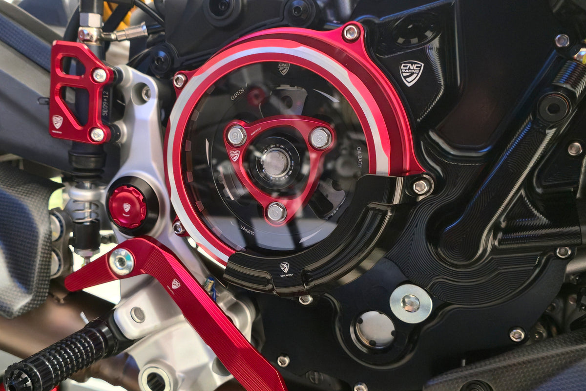 CNC Racing transparant koppelingsdeksel CA511BR met zwarte CAP03B beschermer gemonteerd op Ducati 890cc V2 – close-up van de complete montage met zicht op koppeling en voetsteun.